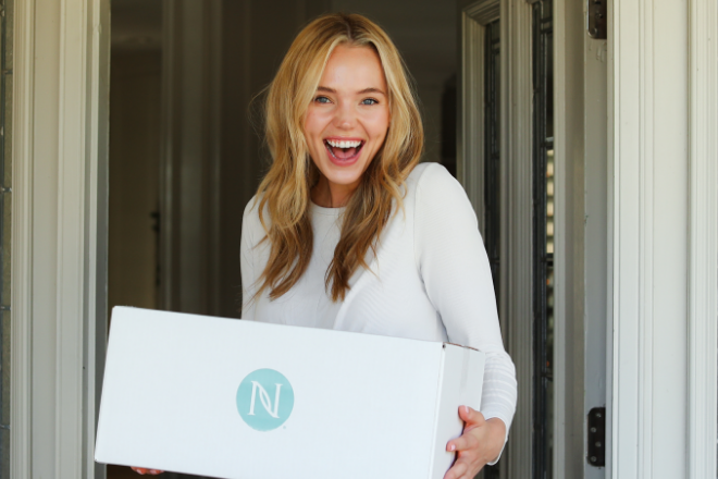 Woman smiling and holding a Neora package at front door step.